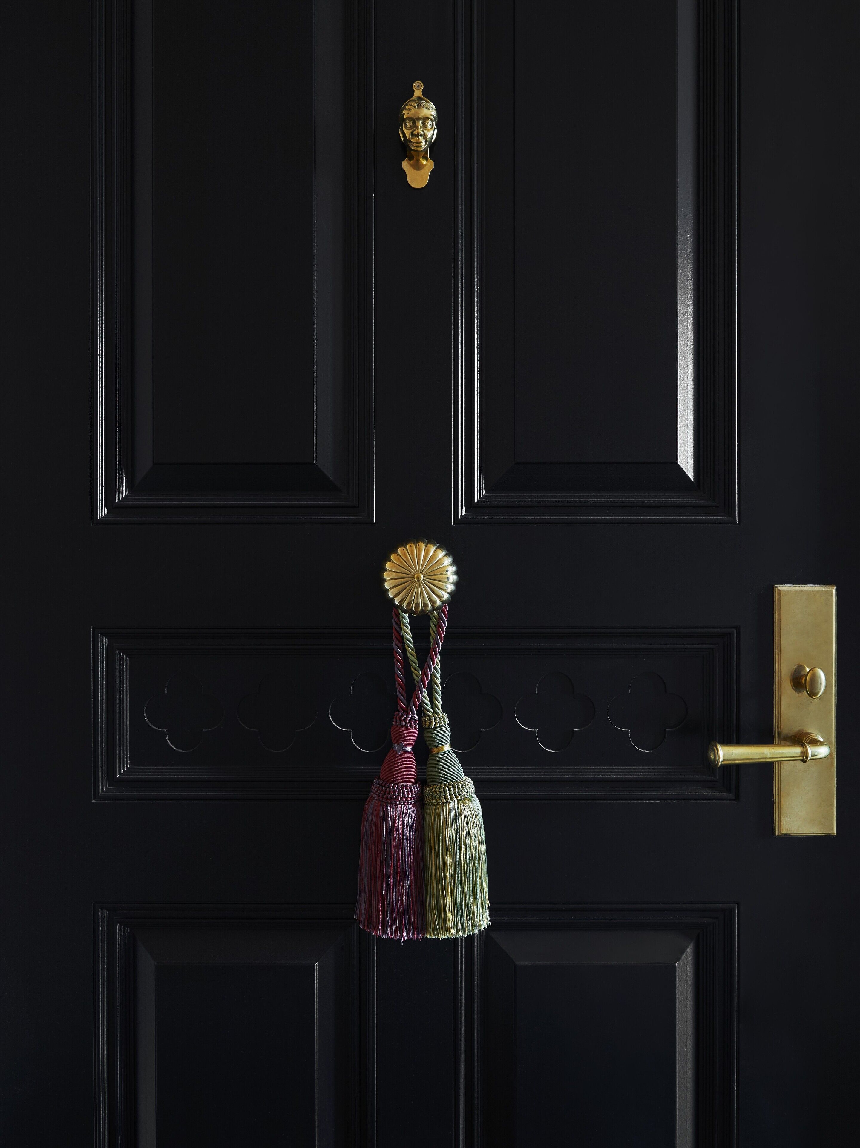 A black door with a brass doorknob, a brass handle, and a decorative tassel.