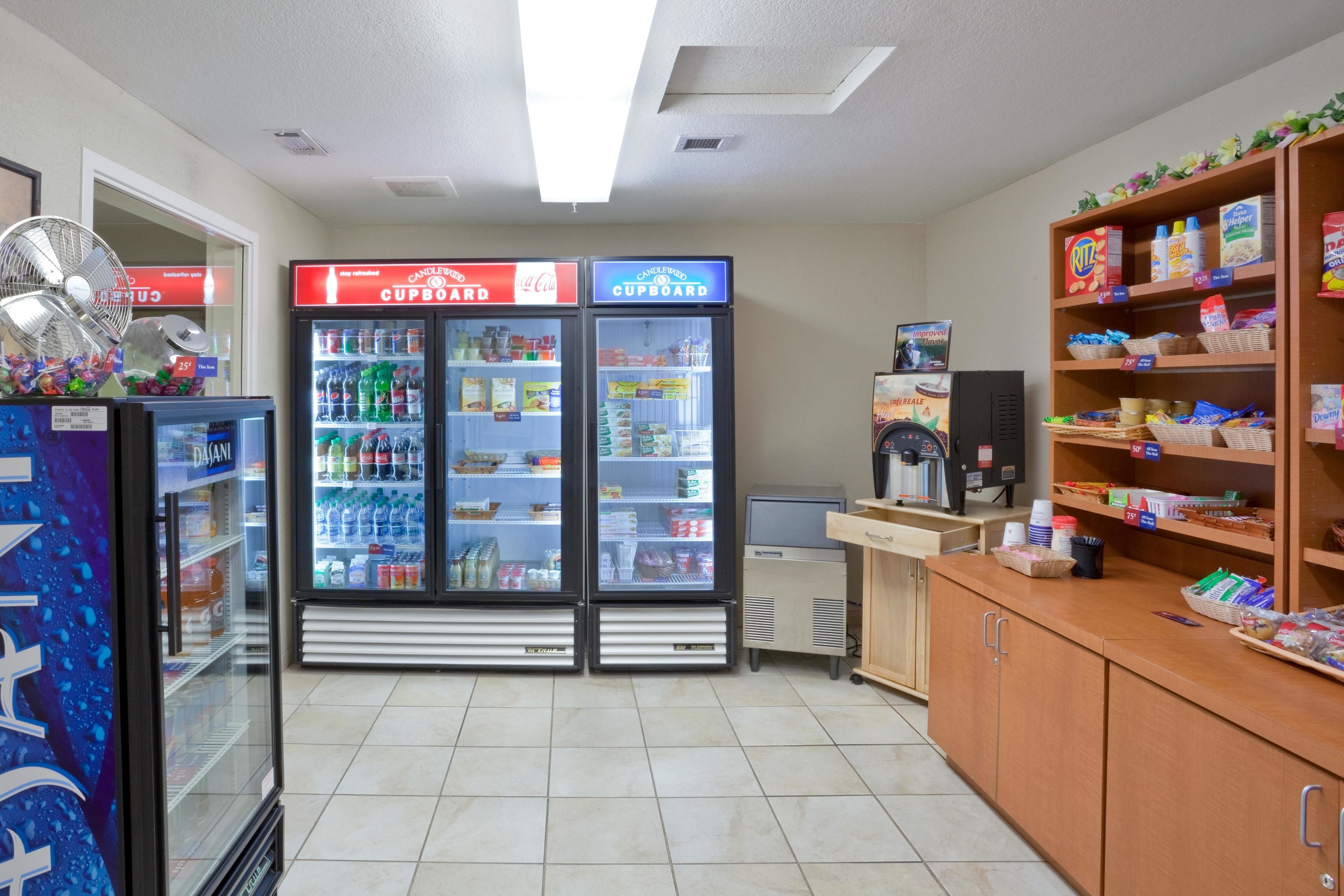A convenience store with refrigerated beverage displays, a fan, and shelves stocked with snacks and household items.