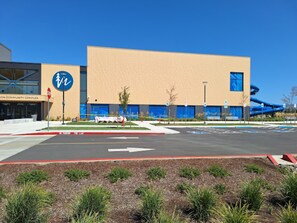 A modern building with a large blue logo, a parking lot, and a landscaped area with shrubs. - Candlewood Suites Medford by IHG (Medford)
