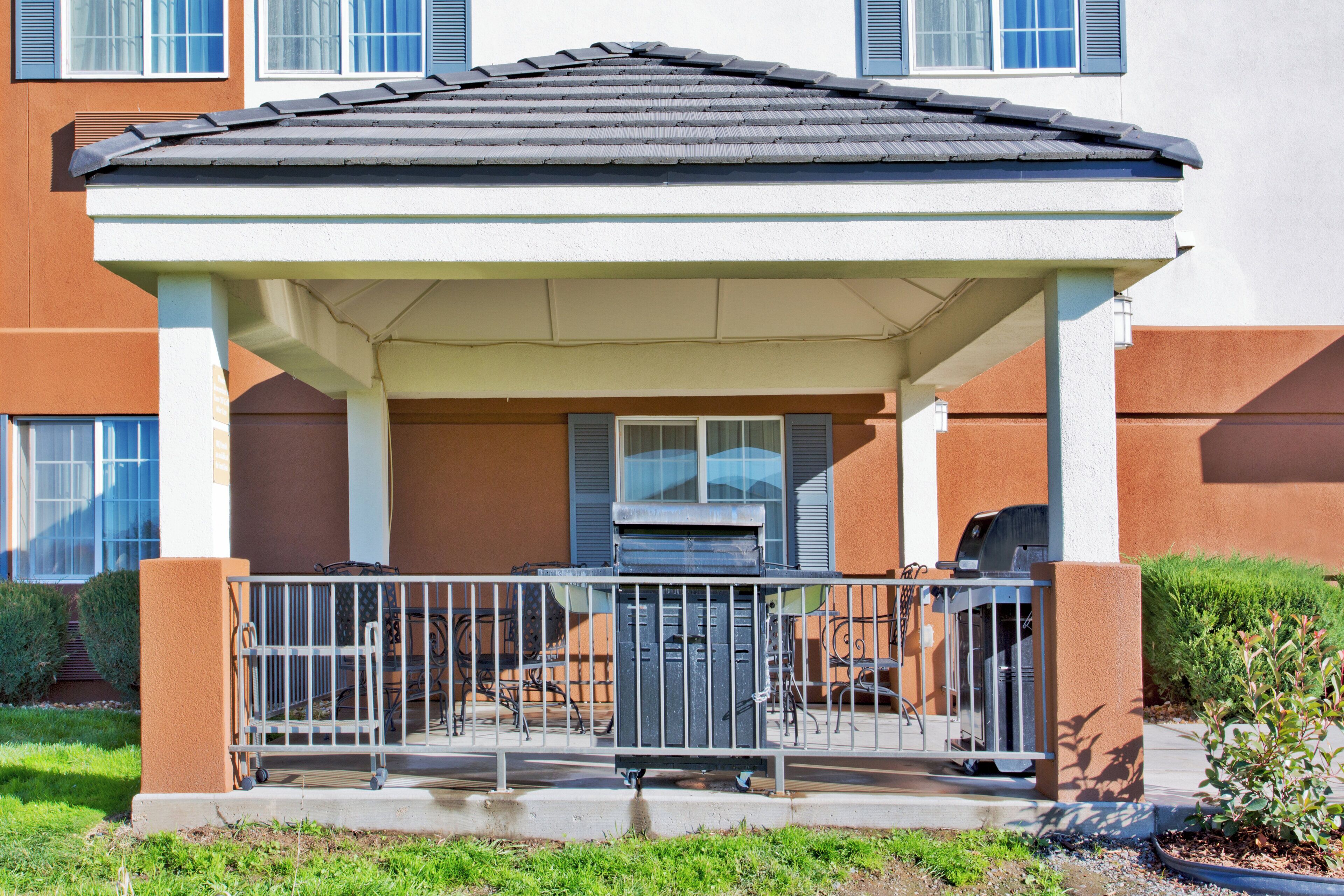A covered outdoor seating area with a metal railing, a grill, and a window.