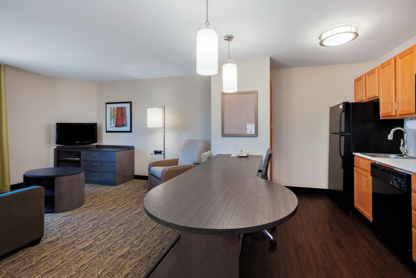 A modern hotel room with a dining table, a sofa, a TV, a desk, and a kitchen area with a refrigerator and dishwasher. - Candlewood Suites Medford by IHG (Medford)