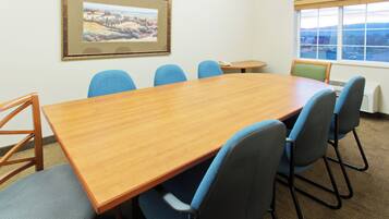 Un salón de conferencias con una mesa de madera, sillas azules, una mesa redonda pequeña, un teléfono y una ventana con vistas.