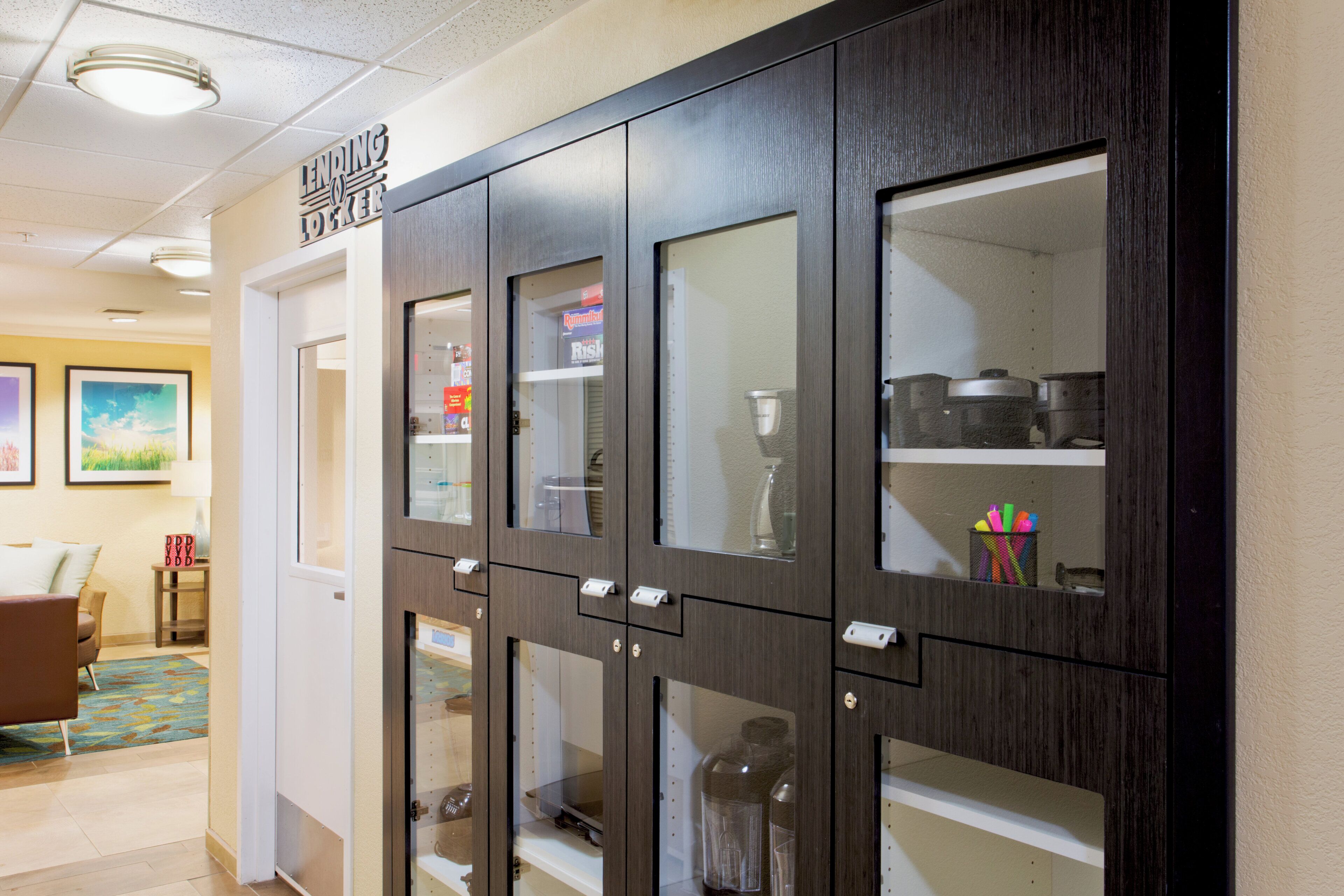 A hallway with a dark wooden cabinet with glass doors, a door with a sign above it, and a small table with a lamp.