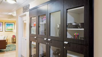 A hallway with a dark wooden cabinet with glass doors, a door with a sign above it, and a small table with a lamp.