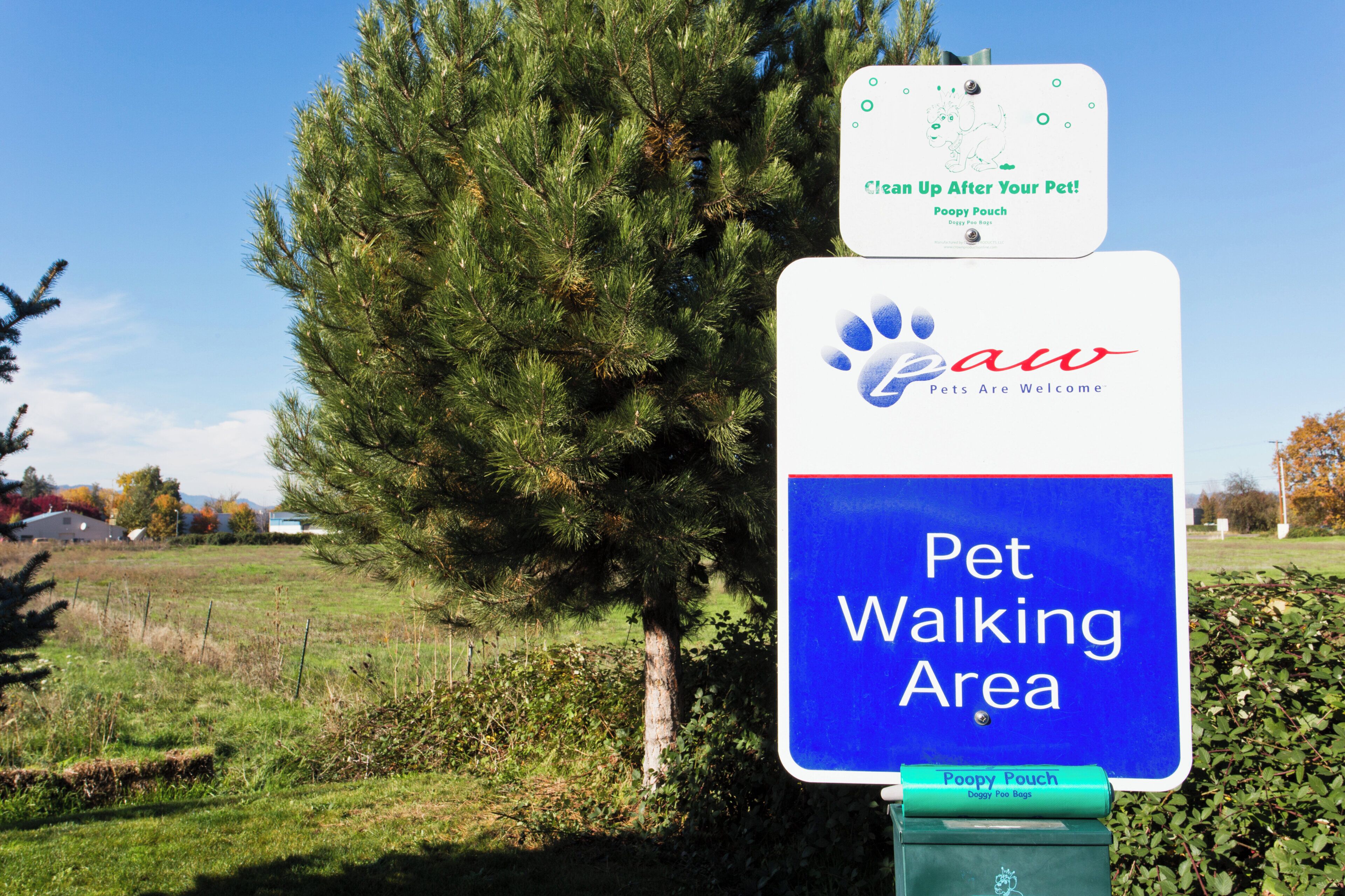 A sign indicating a pet walking area with a paw print logo and a doggy poo bag dispenser.