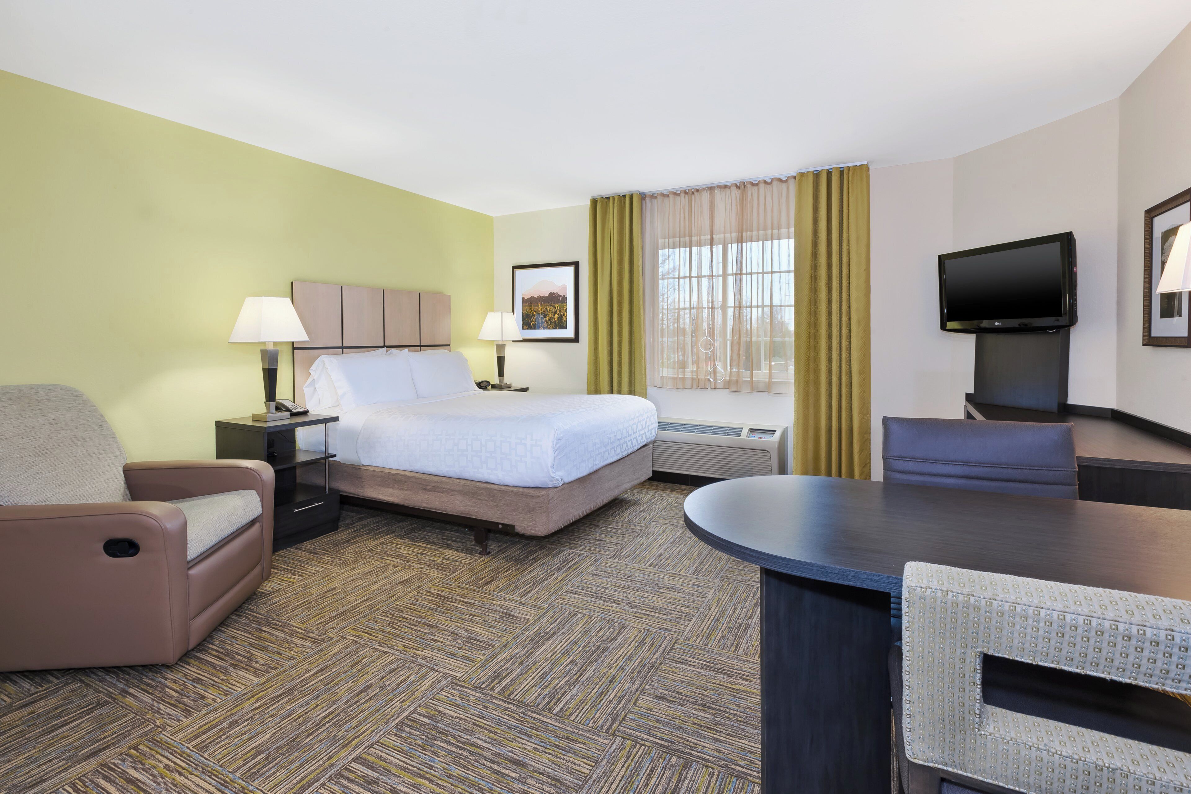 A hotel room with a bed, two bedside tables, a desk, a chair, a television, and a window with curtains.