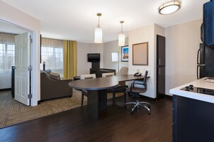 Quarto de hotel moderno com área de jantar, sofá, televisão e bancada de cozinha.