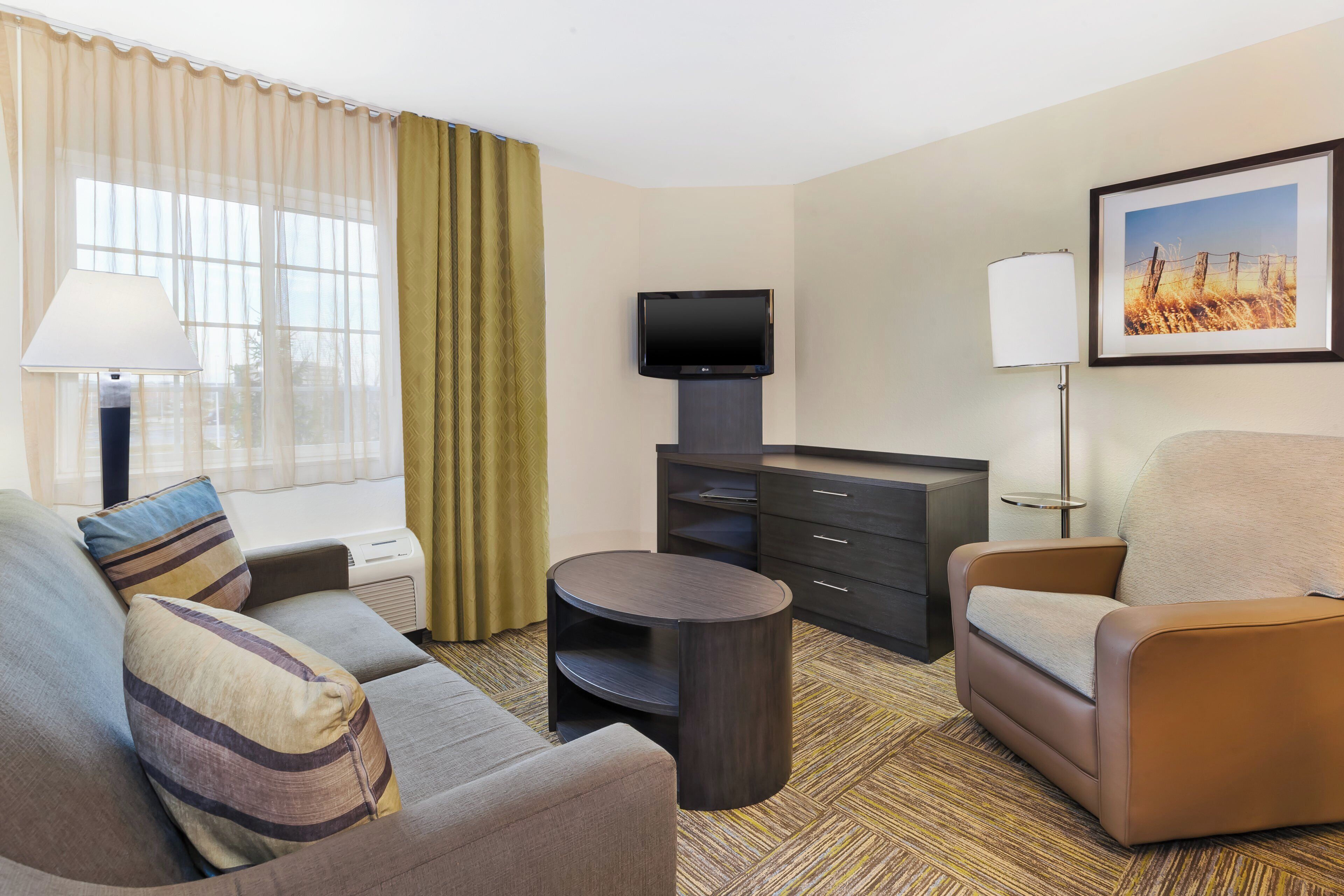 A hotel room with a sofa, armchair, TV, and a small table.