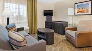A hotel room with a sofa, armchair, TV, and a small table. - Candlewood Suites Polaris by IHG (Columbus)