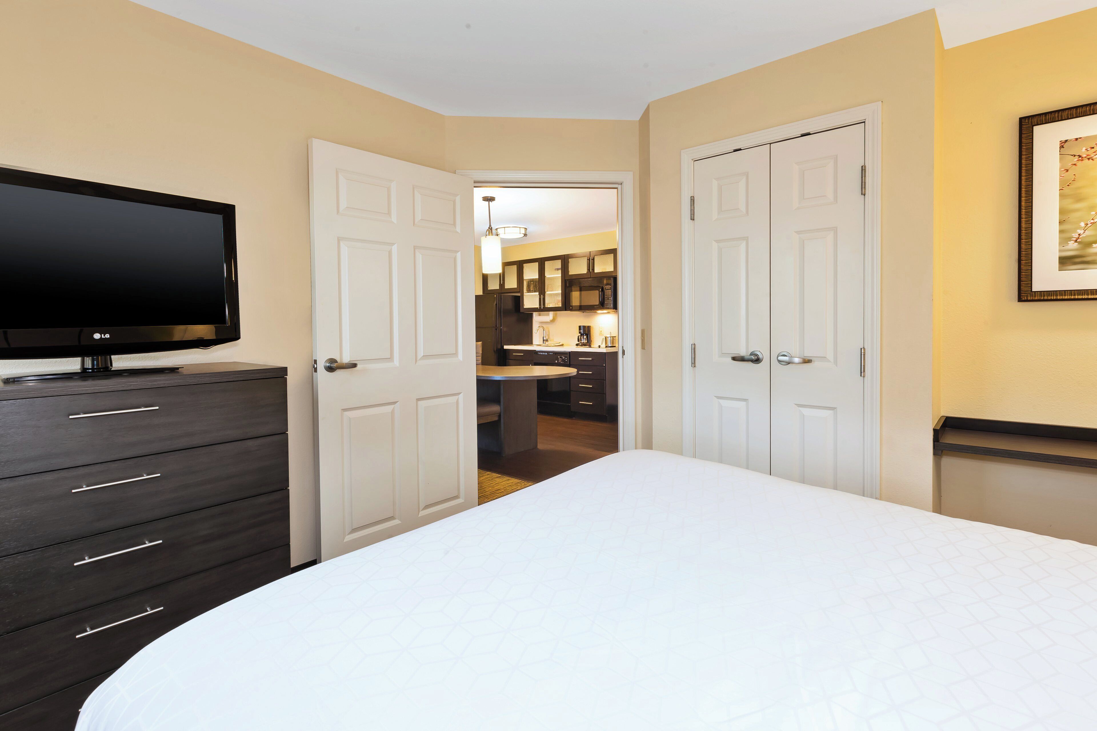 Un dormitorio con cama, televisor, cómoda y puerta que da al baño.