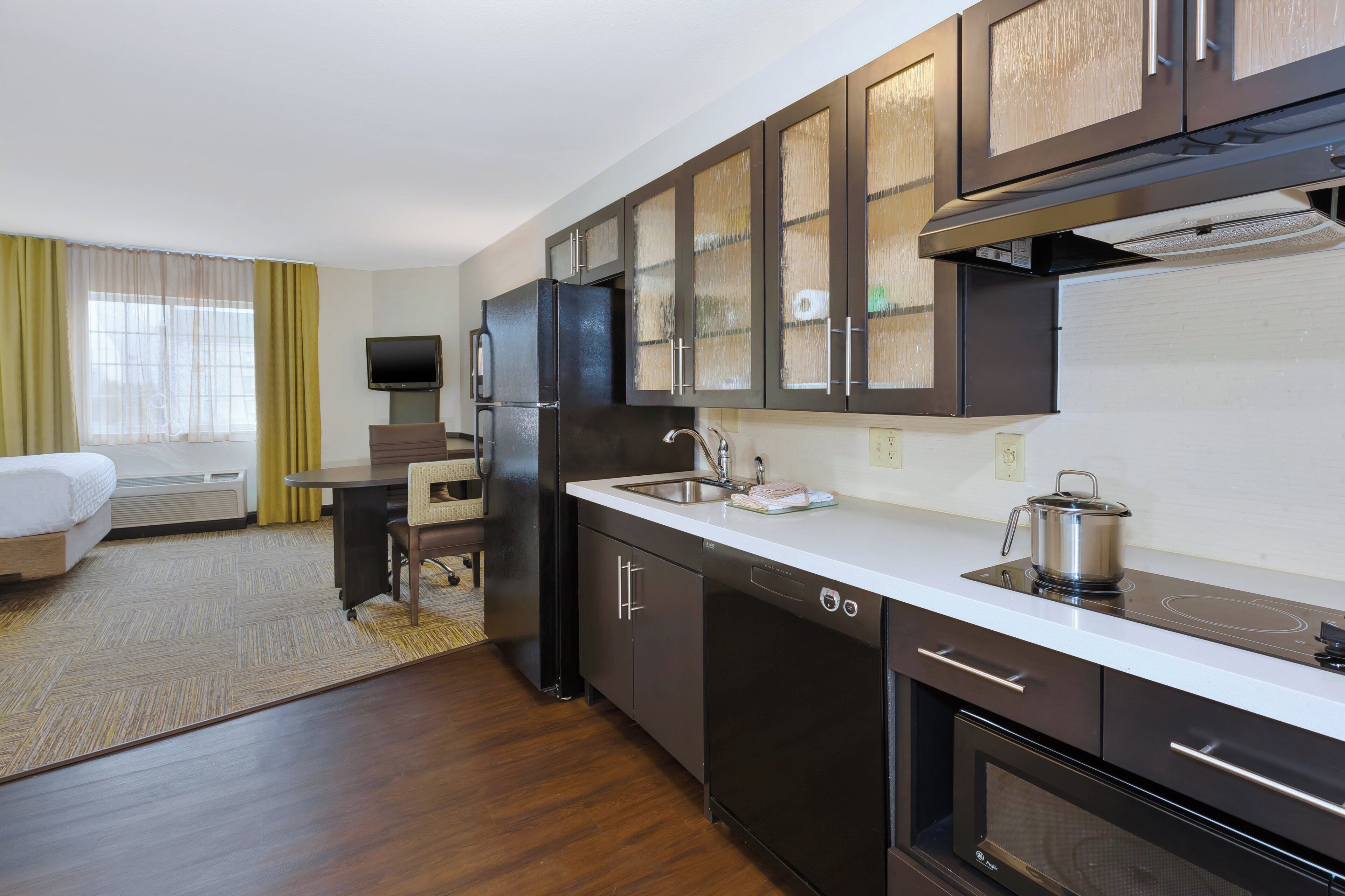 A compact hotel kitchen with a refrigerator, stove, microwave, and a sink.
