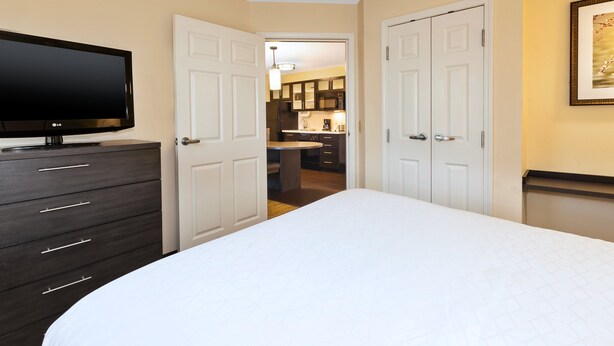 A bedroom with a bed, a dresser, a TV, and a door leading to a bathroom. - Candlewood Suites Polaris by IHG (Columbus)