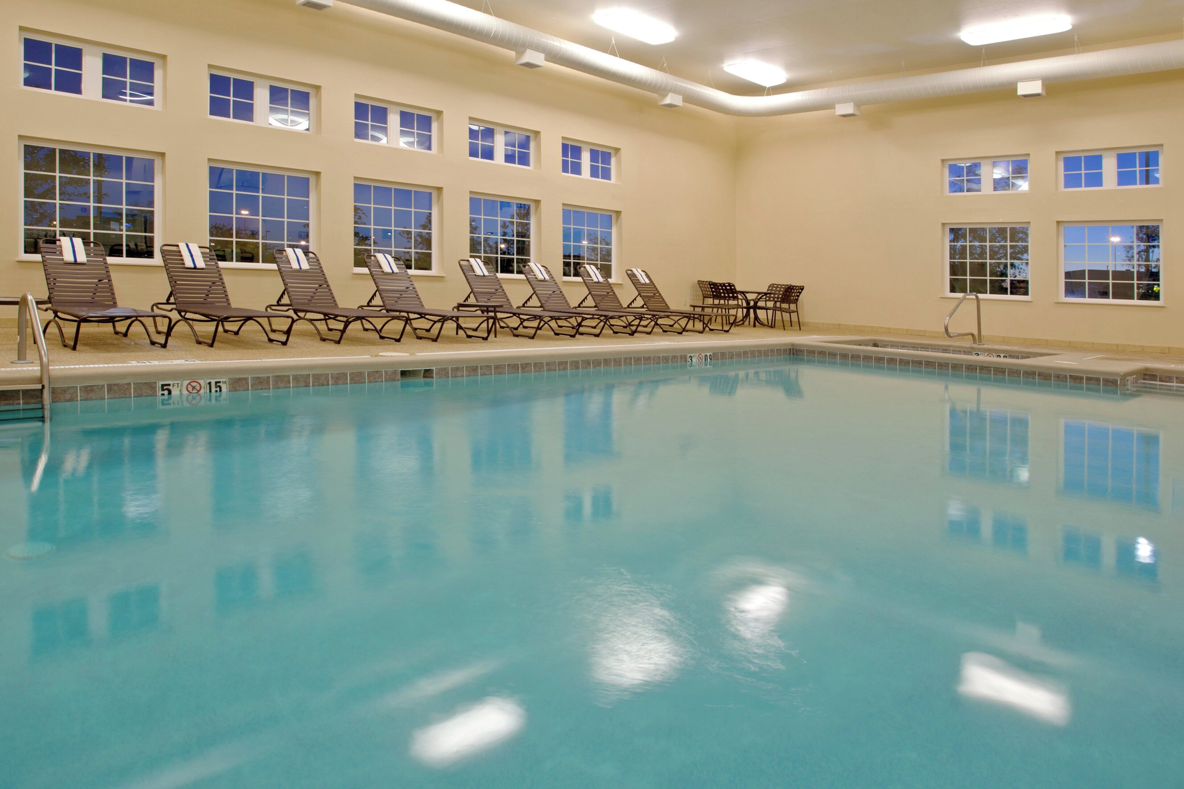 A swimming pool with lounge chairs and a sunbed area, surrounded by windows.