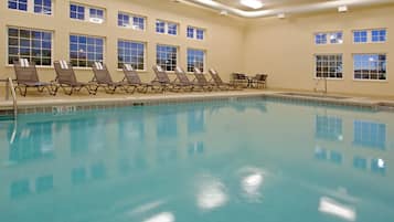 A swimming pool with lounge chairs and a sunbed area, surrounded by windows.