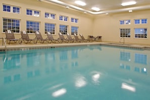 A swimming pool with lounge chairs and a sunbed area, surrounded by windows.