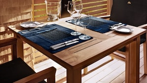 Une table de salle à manger en bois, mise avec des sets de table bleus, des verres à vin et des couverts.