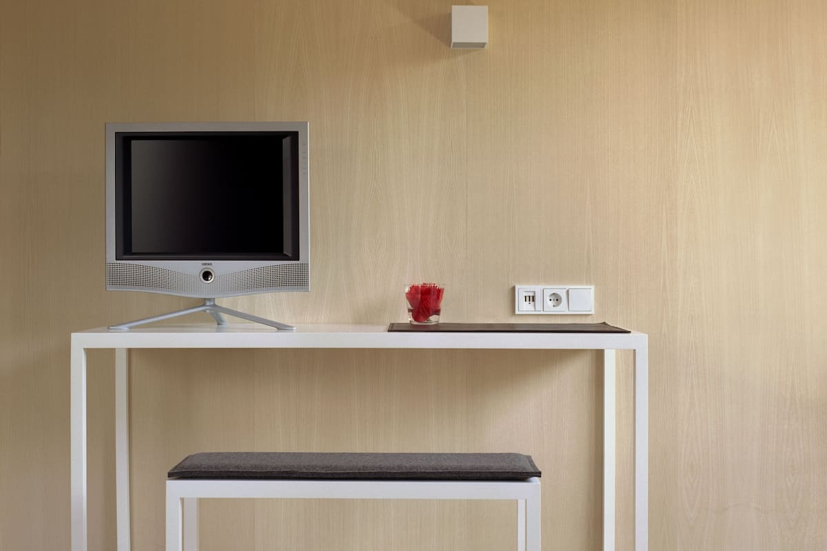 Habitación minimalista con un escritorio blanco, un televisor de pantalla plana, un florero rojo y una toma de corriente.