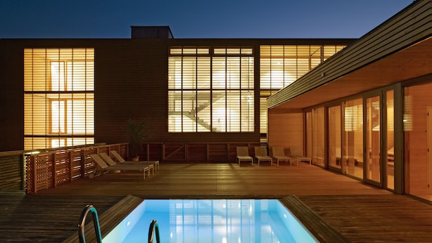 Un espace piscine extérieur moderne, doté d’une terrasse en bois, de chaises longues et d’un jacuzzi protégé par des parois de verre.