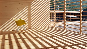Une pièce avec un plancher et des murs en bois, une chaise jaune et une fenêtre donnant sur une montagne et un bâtiment.