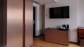 Ein modernes Hotelzimmer mit Holzboden im Fischgrätmuster, einem an der Wand montierten Flachbildfernseher, einer Minibar und einem Holzkabinett.