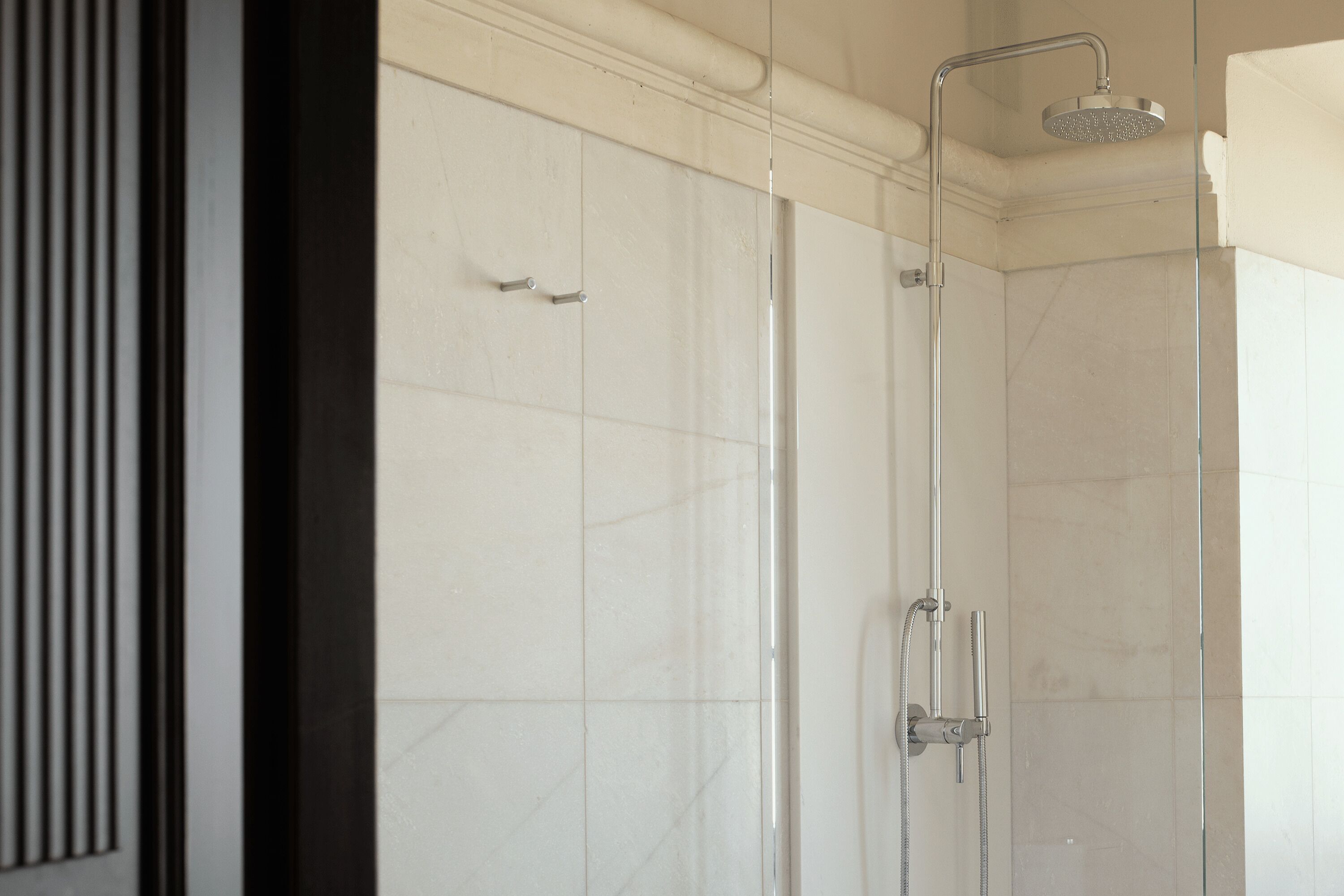 Een moderne badkamer met een glazen douchecabine, witte betegelde wanden en een zichtbaar deurklink.