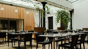 Un comedor amplio con varias mesas y sillas, ventanas grandes y plantas colgantes.