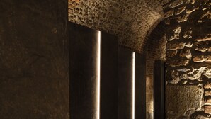 Un pasillo con paredes y columnas de piedra, con una serie de franjas verticales de luz iluminada.