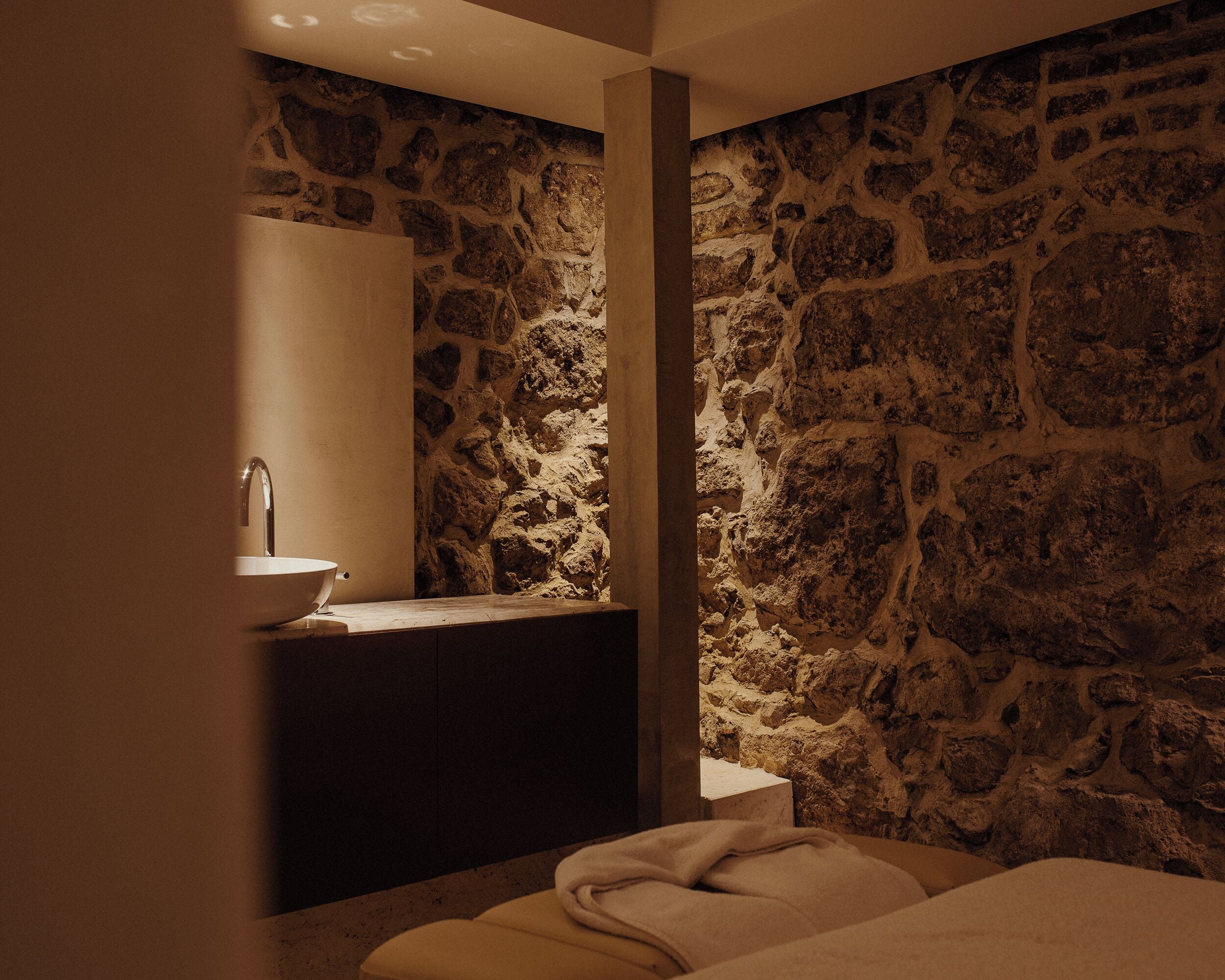 Une salle de bain avec un mur en pierre, un lavabo et un miroir.