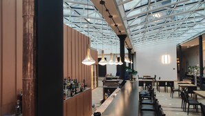 Un bar moderno con techo alto y tragaluces, con iluminación colgante y una larga barra con taburetes.
