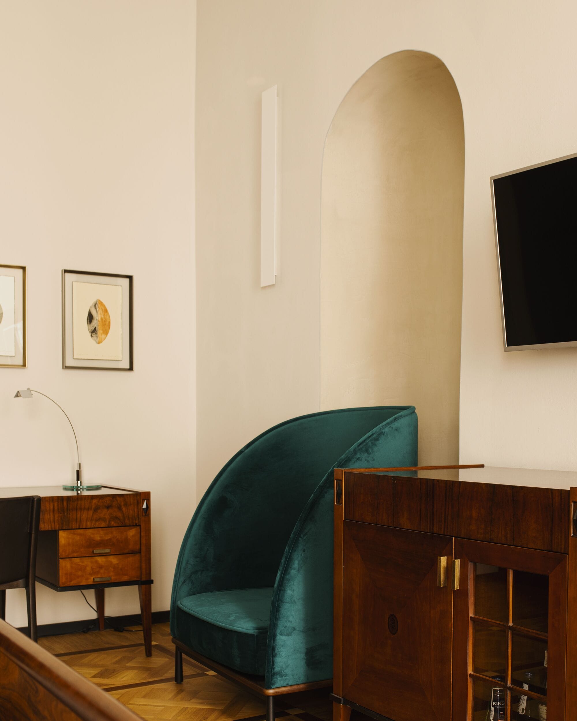 A room with a teal armchair, a wooden desk, a flat-screen TV, and framed artwork on the wall.