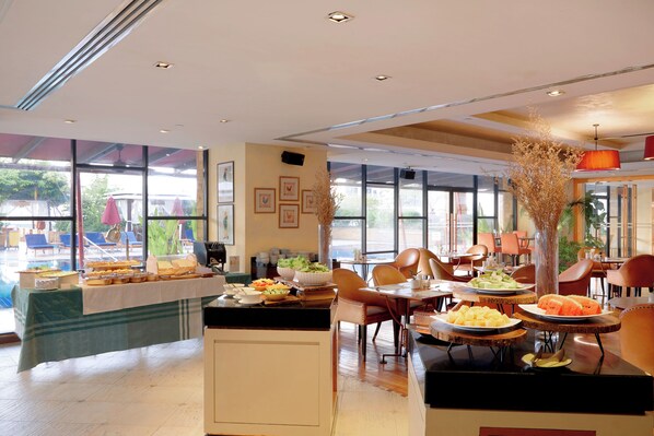 A hotel dining area with a buffet setup, multiple dining tables, and chairs.