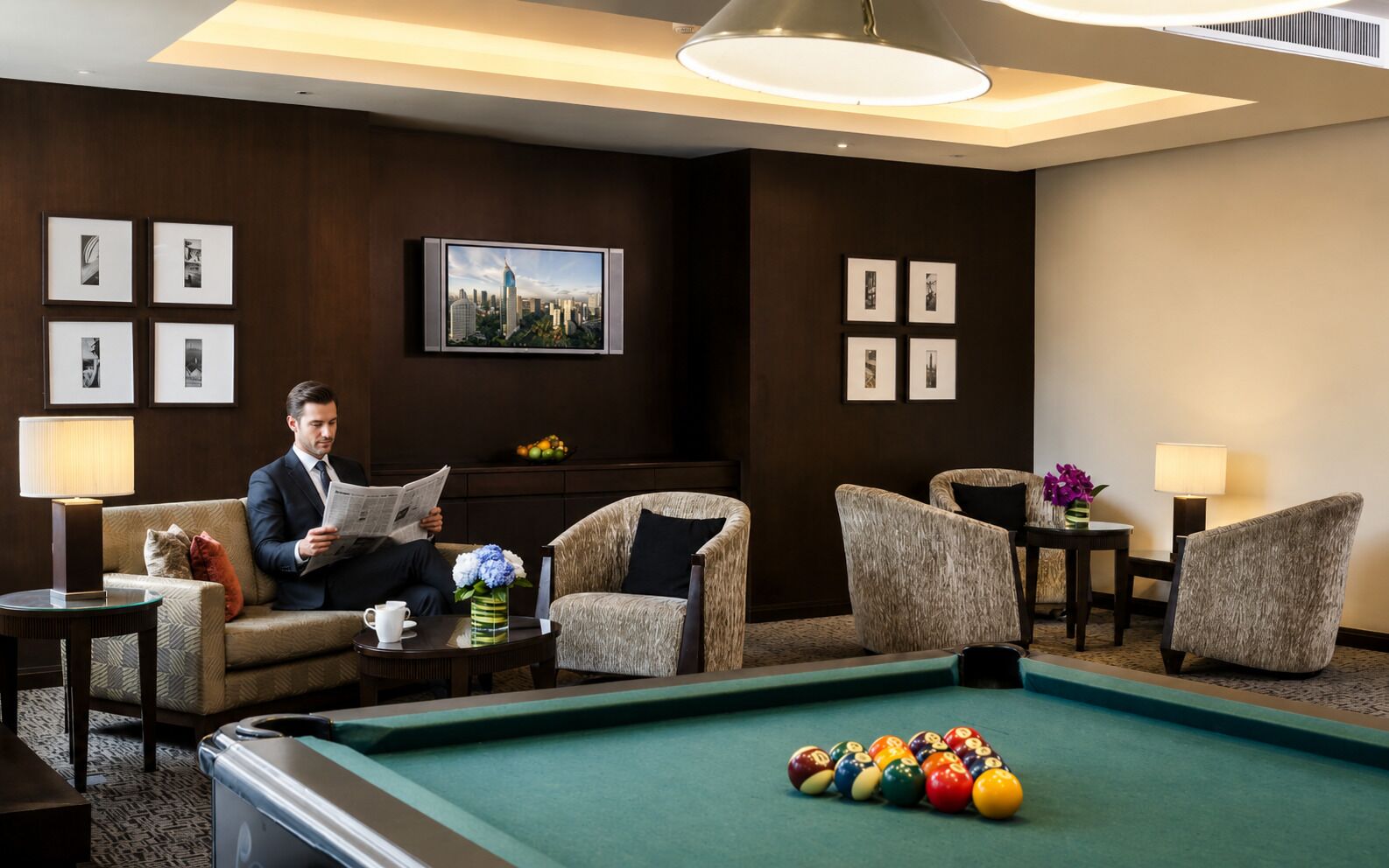 A hotel room with a pool table, a sofa, armchairs, a television, and framed pictures on the wall.