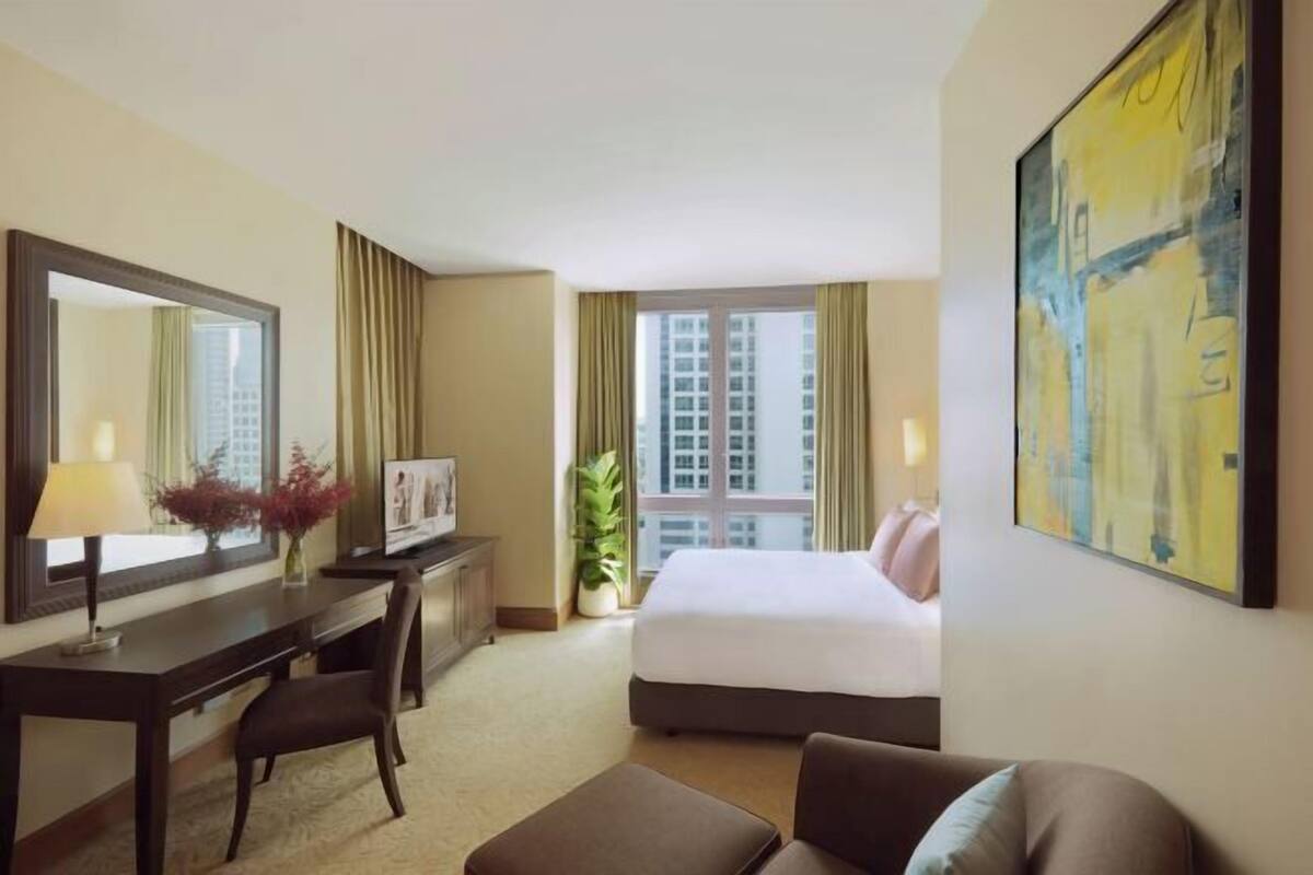 Ein Hotelzimmer mit einem Bett, einem Schreibtisch, einem Sessel, einem großen Spiegel, einem Gemälde und einem Fenster mit Vorhängen.