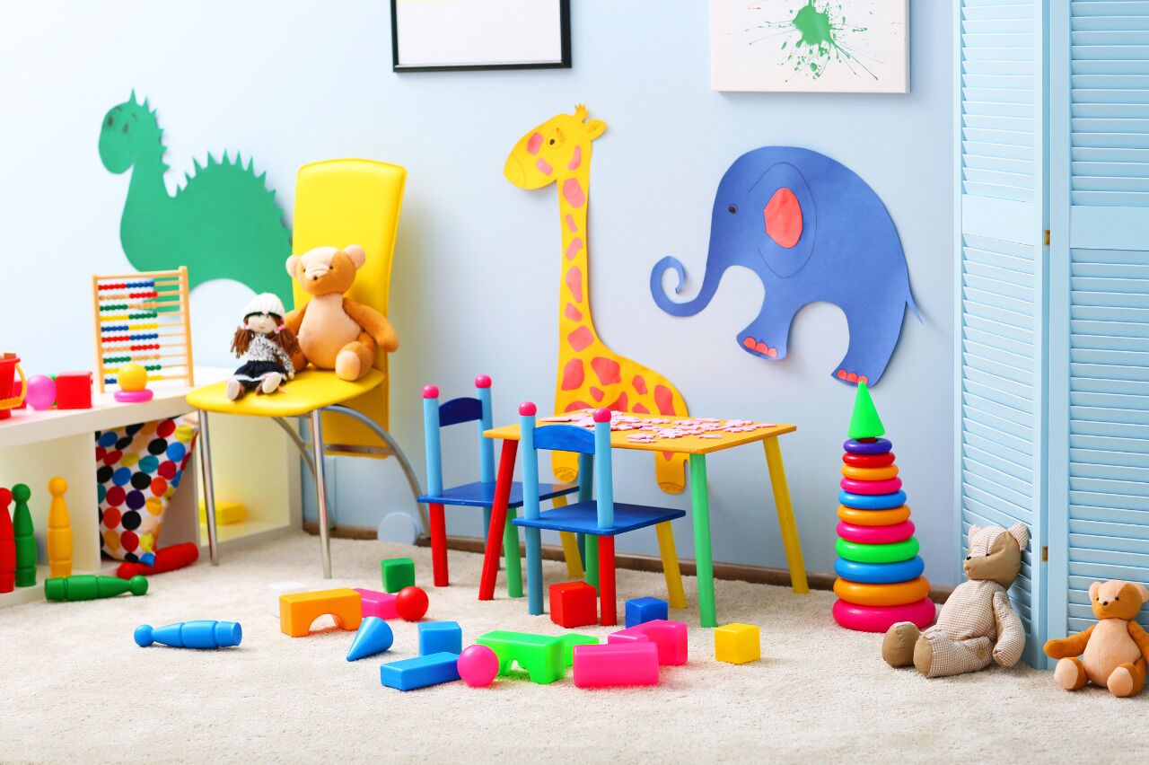 Une salle de jeux pour enfants avec une découpe en forme de dinosaure, une girafe, un éléphant et divers jouets éparpillés sur le sol.