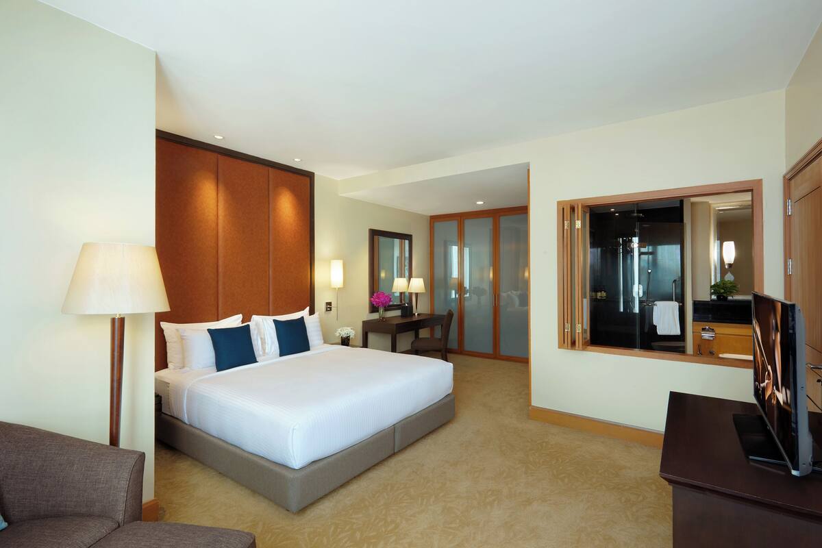 Ein Hotelzimmer mit einem großen Bett, einem Schreibtisch mit Stuhl, einem Fernseher und einem durchgegangene Tür erkennbaren Badezimmer.