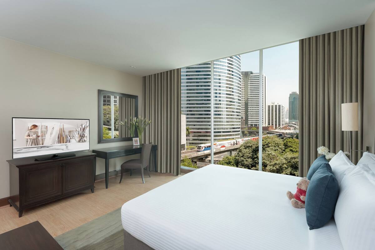 Ein modernes Hotelzimmer mit einem großen Bett, einem Schreibtisch, einem Fernseher und Blick auf die Stadt.