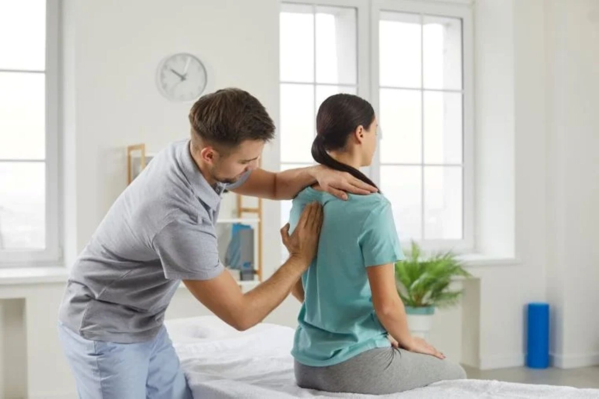 A person receiving a neck adjustment from another individual in a room with a clock on the wall.