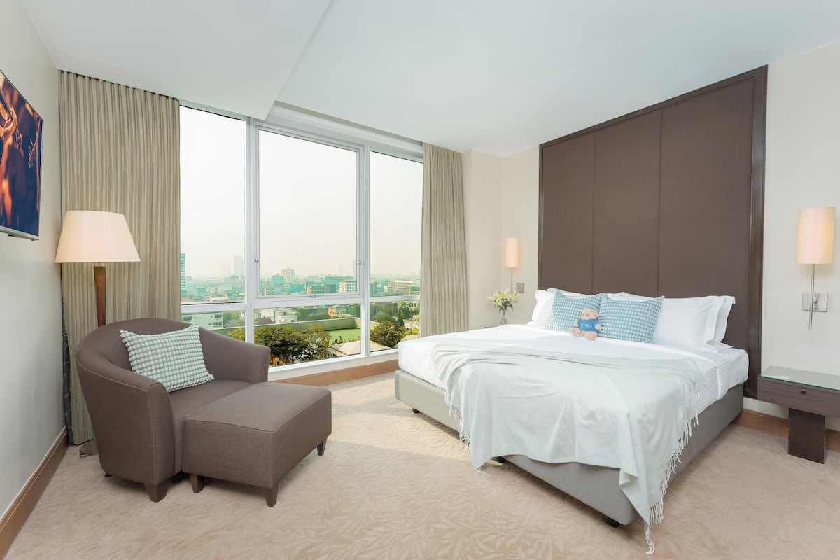 Ein Hotelzimmer mit einem großen Bett, einem Sofa, einem Fenster mit Stadtblick und einem Nachttisch.