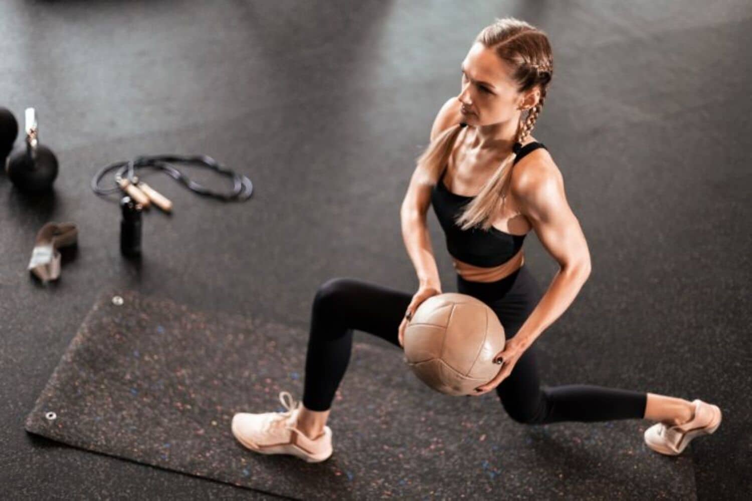 Una persona realizando un ejercicio de estiramiento con una pelota medicinal sobre una colchoneta en un gimnasio.