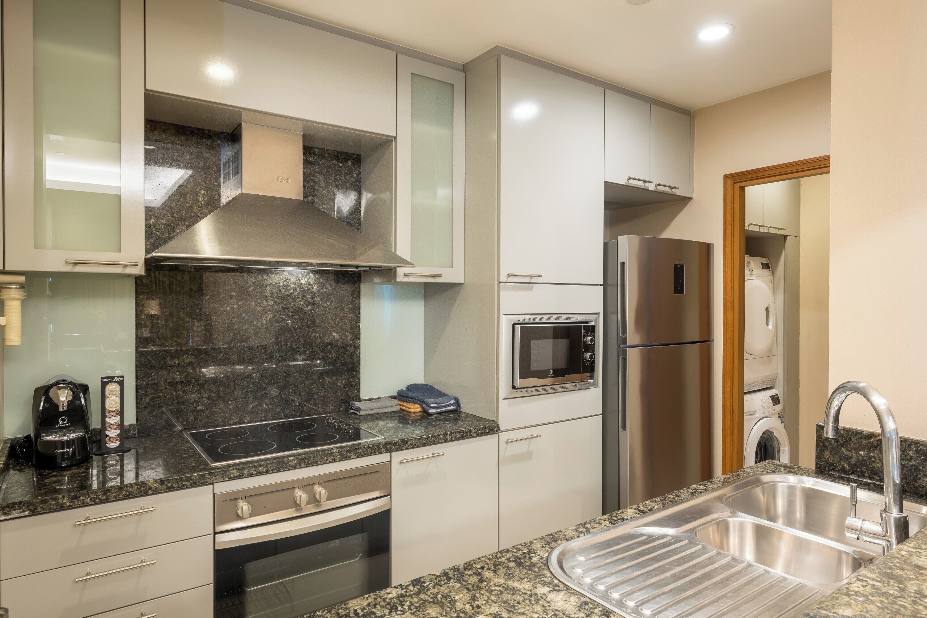 A modern kitchen with a stainless steel range hood, built-in microwave, and a double sink.