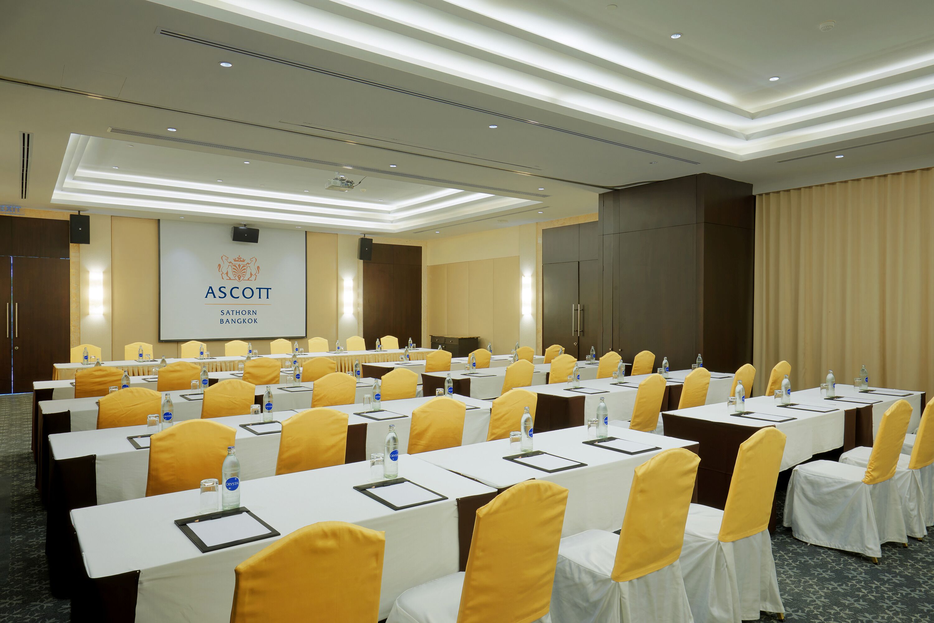 A conference room with rows of tables and chairs, a podium, and a projection screen.