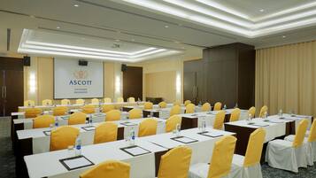 A conference room with rows of tables and chairs, a podium, and a projection screen.