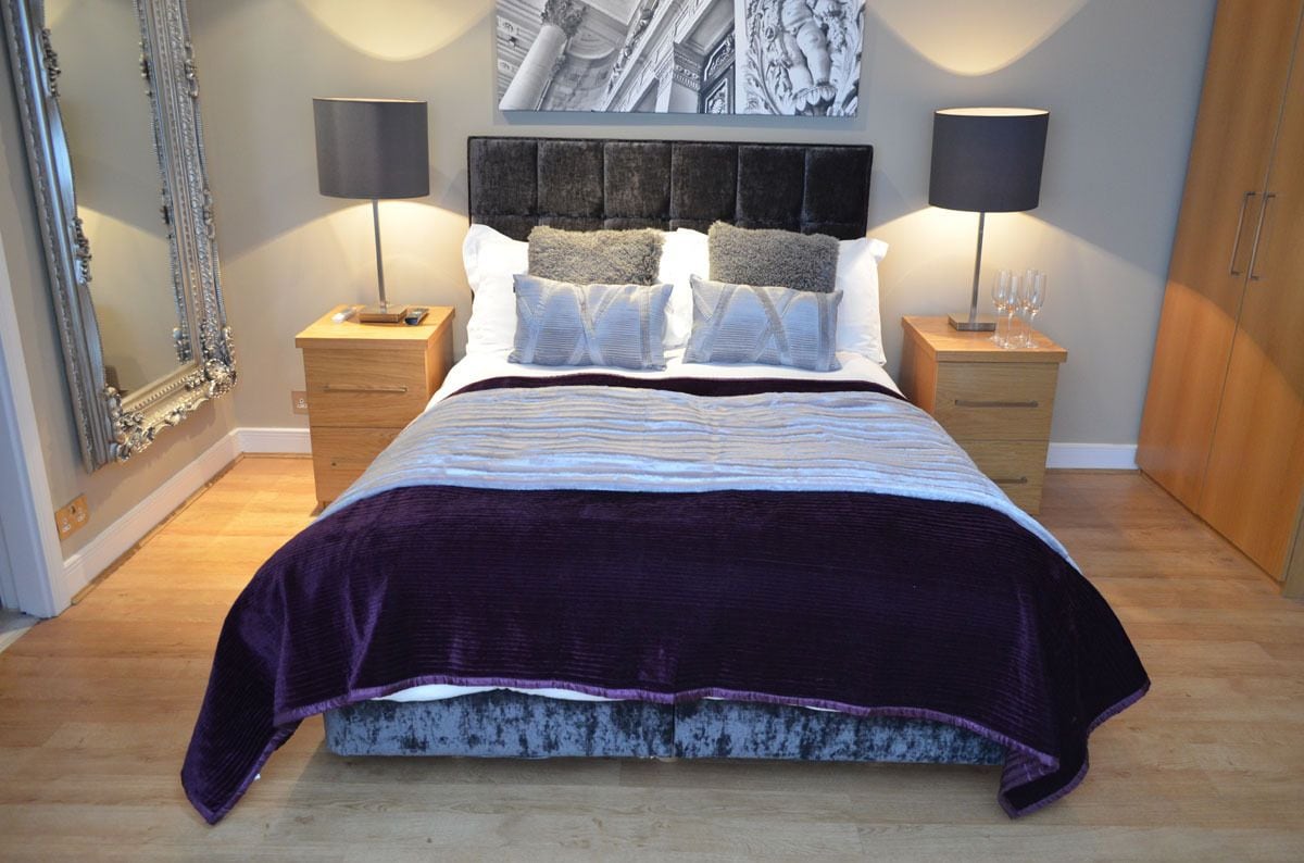 A bedroom with a large bed, two nightstands, a dresser, a mirror, and wall art.