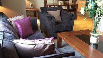 A modern living room with a dark grey sofa, a wooden coffee table, and a dining area with wooden chairs and a table.