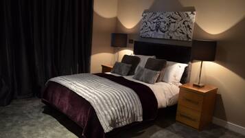 A bedroom with a bed, two bedside tables, a nightstand, a large abstract artwork above the bed, and a dark curtain.