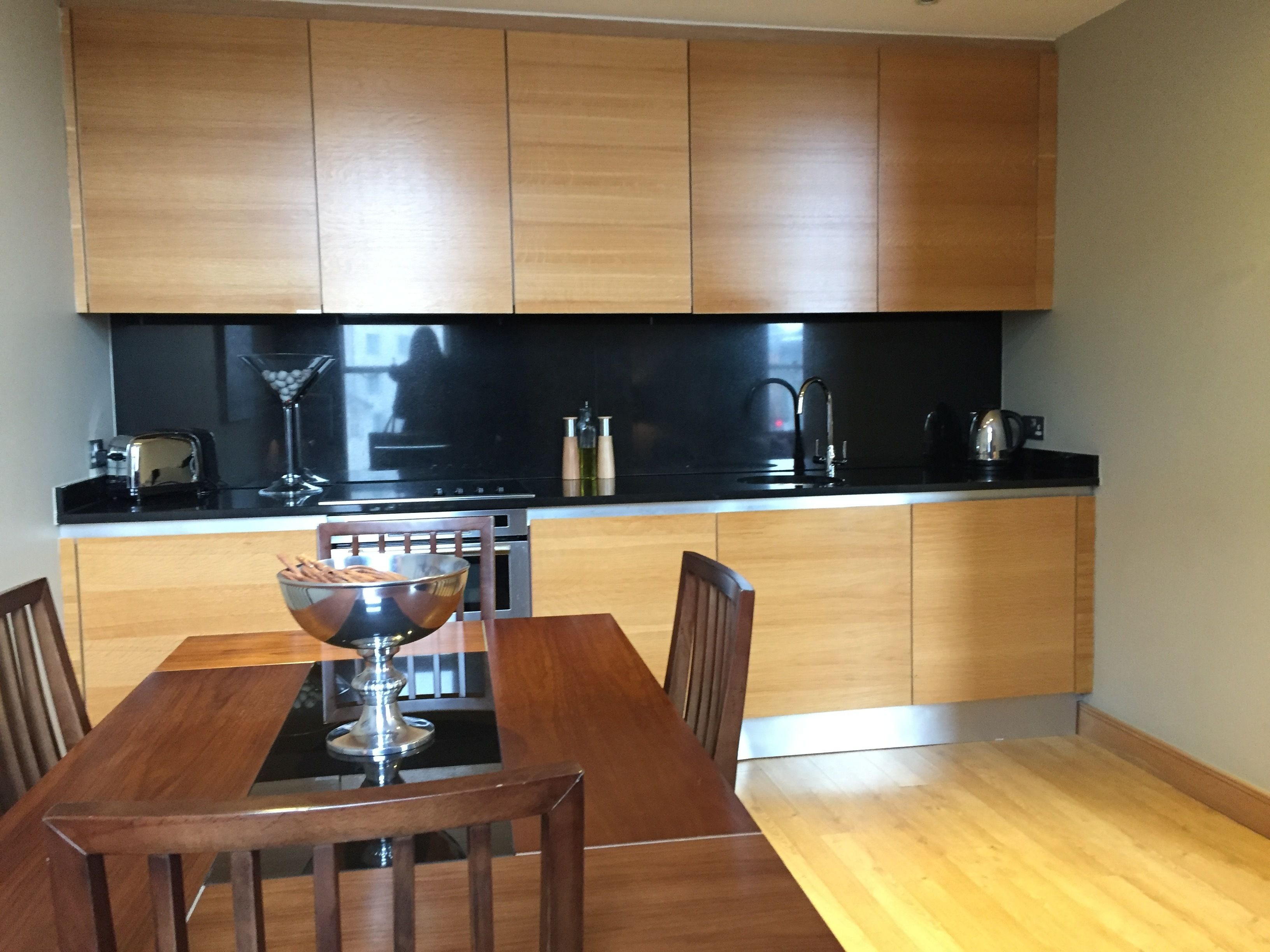 A modern kitchen with wooden cabinets, a black countertop, a dining table with chairs, and a bar area with a glass and a martini glass.