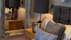 Ein Hotelzimmer mit einem großen, verzierten Spiegel, einem Bett mit vielen Kissen, einem Nachttisch mit Lampe und einem Eimer Champagner.