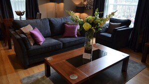 Ein modernes Wohnzimmer mit einem dunkelgrauen Sofa, violetten Kissen, einem Holztisch und einer Vase mit Blumen.