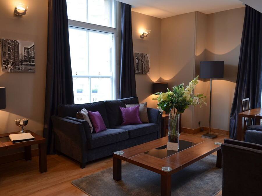 Una sala moderna con un sofá oscuro, una mesa de centro de madera y un jarrón con flores.
