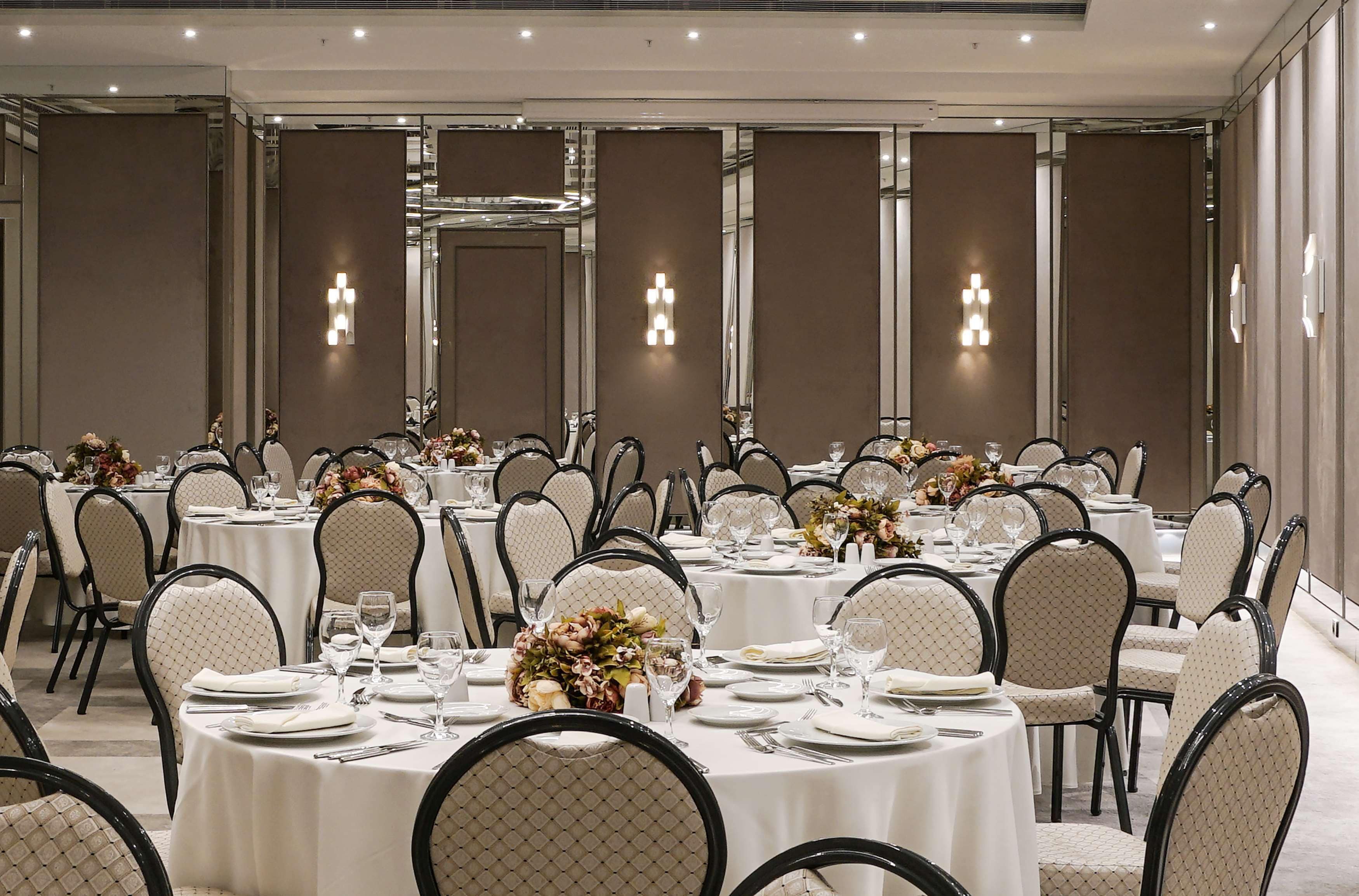 A banquet hall with round tables, chairs, and floral centerpieces.